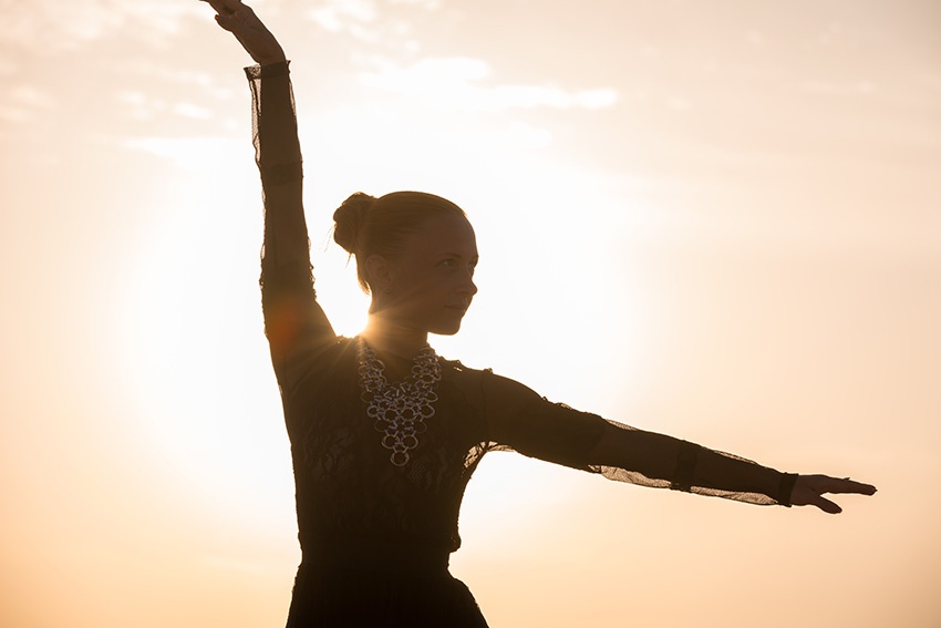 Silhouette of woman dancing gracefully with sun behind her shoulder